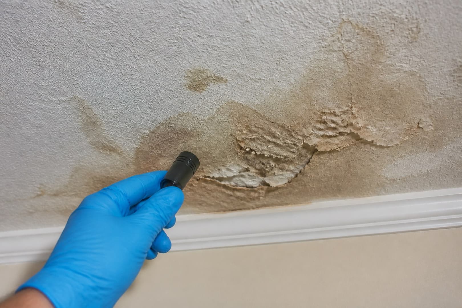 BRG technician measuring moisture around ceiling water damage below a plumbing leak — close technical detail