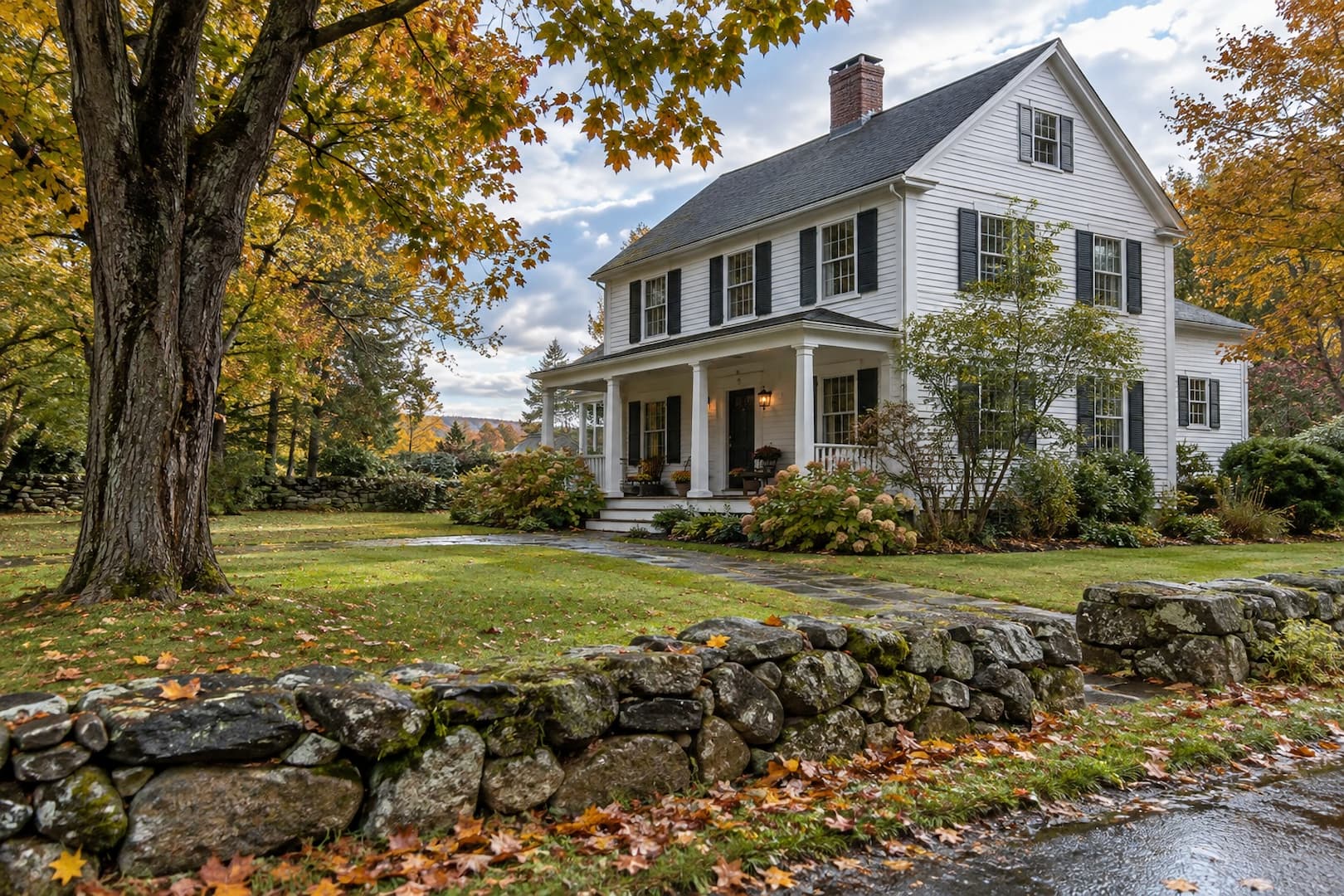 White clapboard home with a stone wall and autumn trees