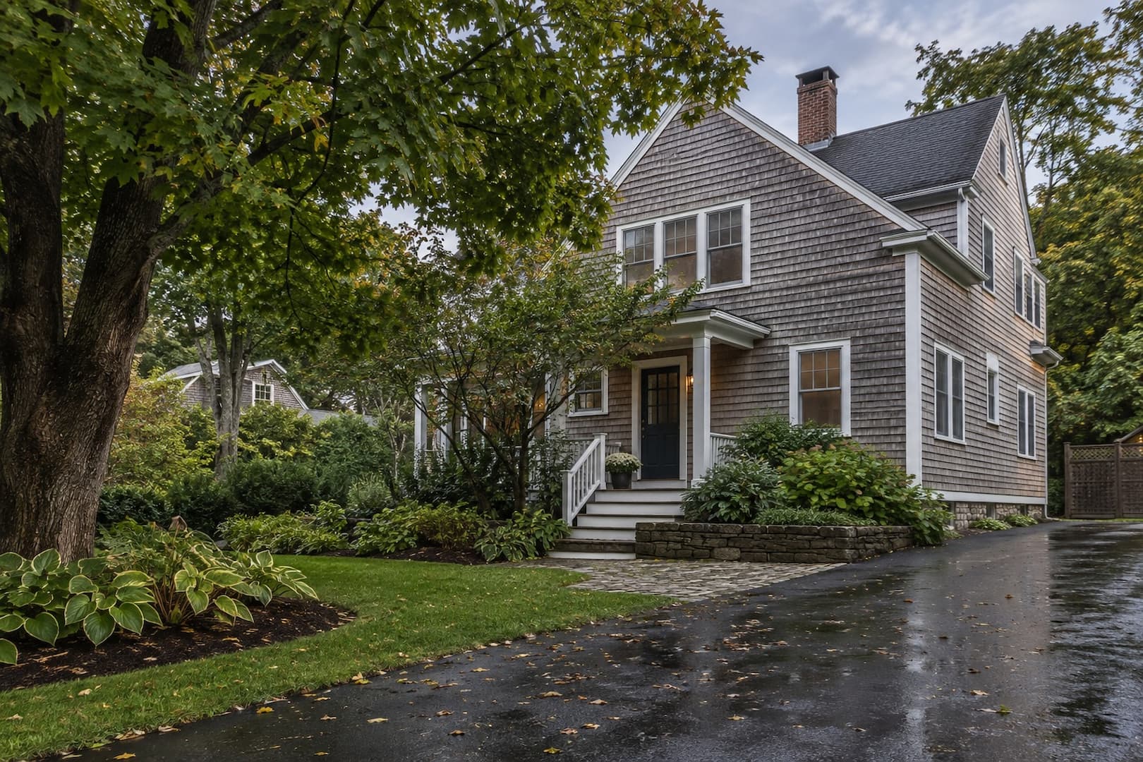 Wooded New England house exterior after rain with a clear driveway and overcast sky